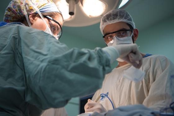 两名医务人员一起在手术台上工作，戴着手术服、帽子和口罩. 
