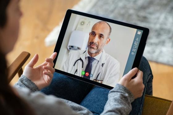 图为一名病人拿着平板电脑，打开视频通话，与医疗专业人员交谈.
