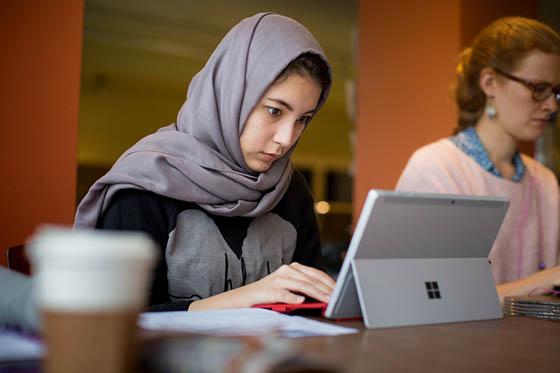 一名波胆网站的学生戴着头巾，在瑞秋咖啡馆的平板电脑上工作