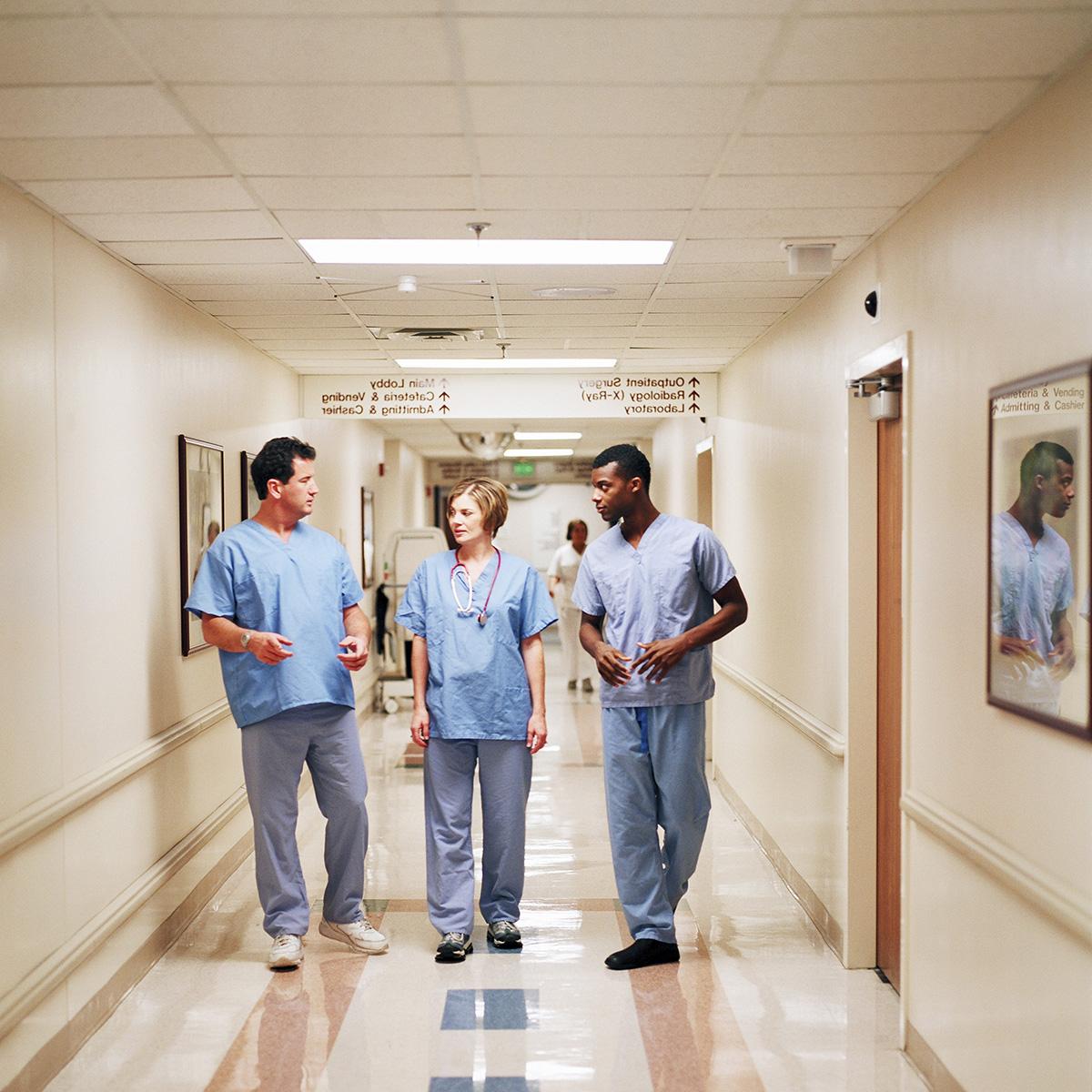 三名护士穿着手术服走过医院走廊的照片
