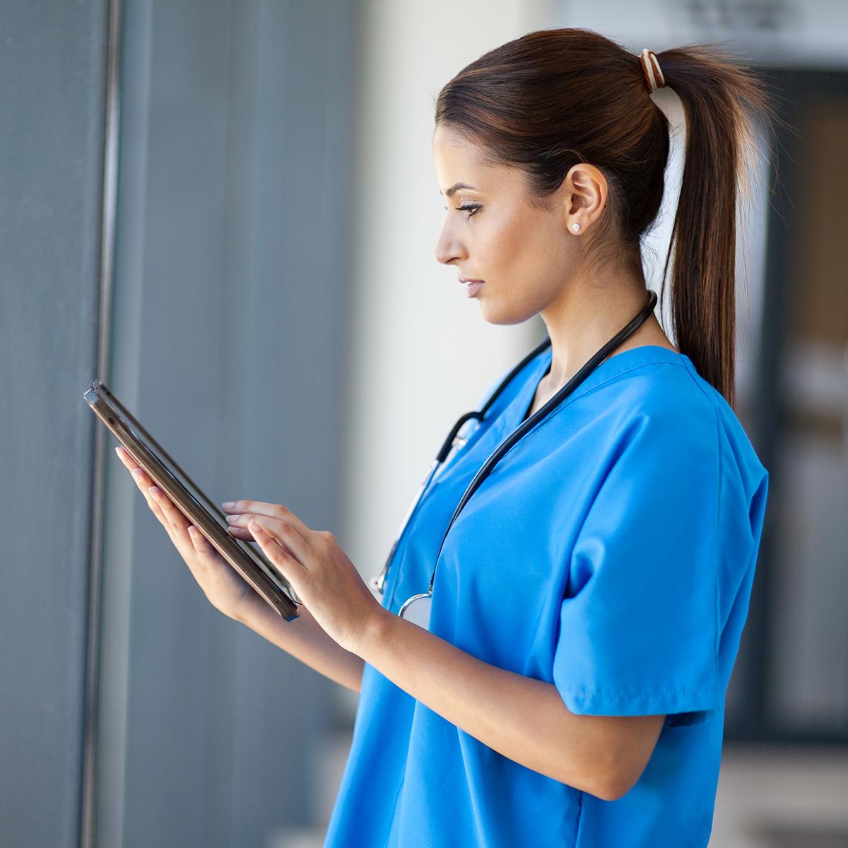 图为一名身穿蓝色工作服的女护士正在阅读平板电脑