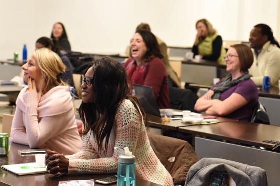 图为一群波胆网站的学生坐在演讲厅里, 微笑着与画框外的教练互动.