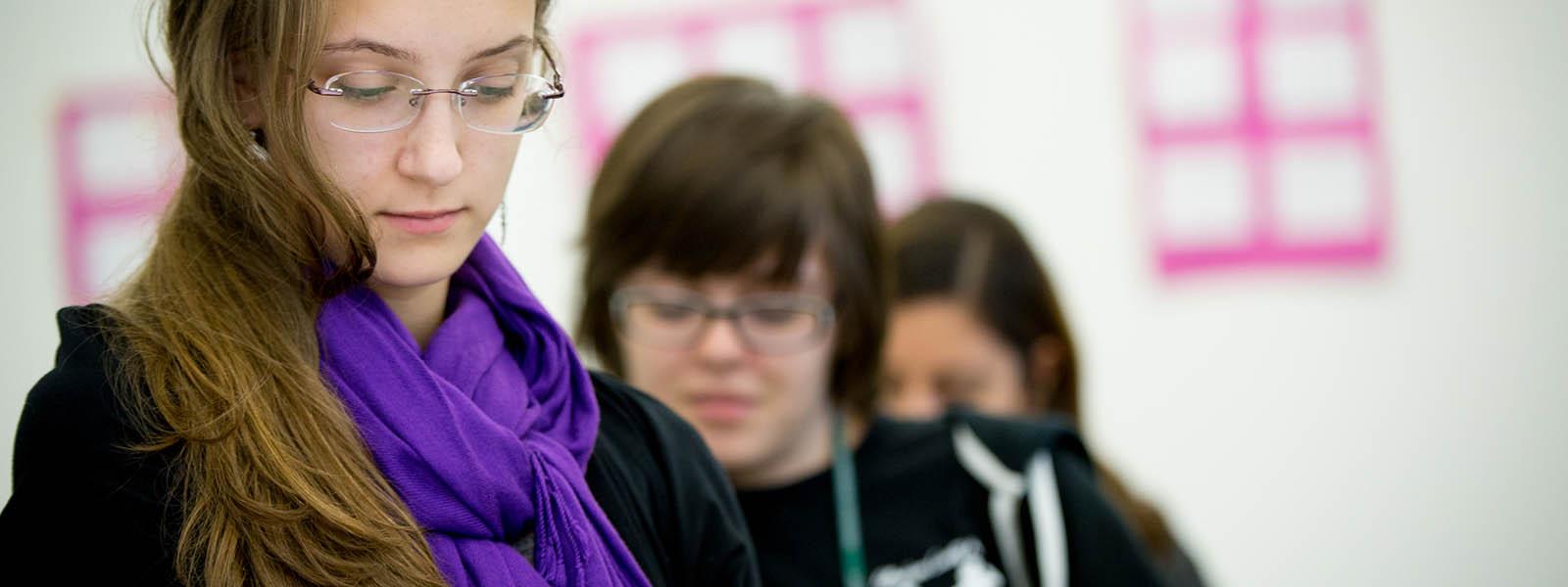 波胆网站的一名学生戴着眼镜，围着紫色围巾，向下看