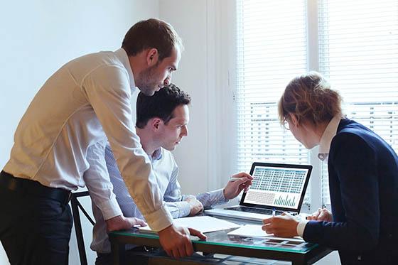 Photo of a group of three business professionals surrounding a computer, 一起完成一个项目.