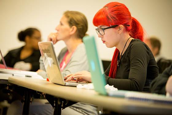 照片中的学生戴着眼镜，头发鲜红, 在波胆网站的演讲厅里用笔记本电脑工作