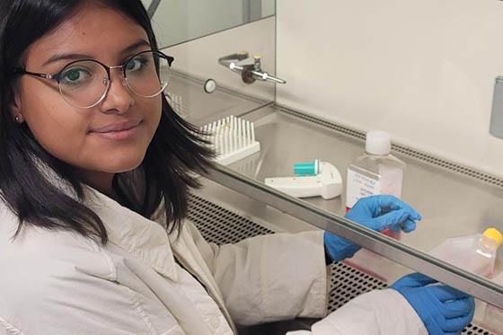 一个戴眼镜的年轻女子的照片, 穿着实验服戴着蓝色乳胶手套, 在实验室工作时摆姿势拍照