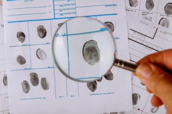 Photo of a h和 holding a magnifying glass over fingerprints