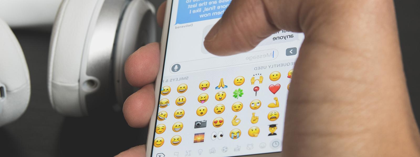 一只手拿着iPhone，在emoji键盘上打字的特写照片.