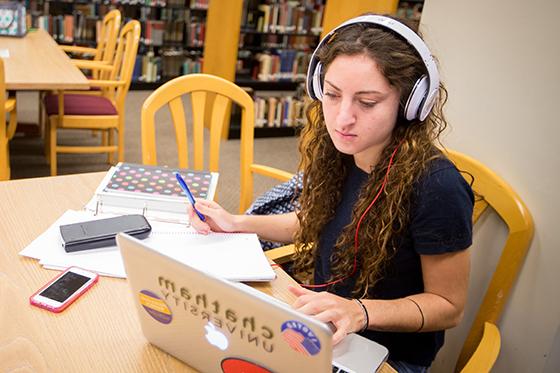 图为一名波胆网站的学生坐在珍妮·梅隆·金图书馆的桌子旁，用笔记本电脑学习，用计算器在笔记本上写字. 