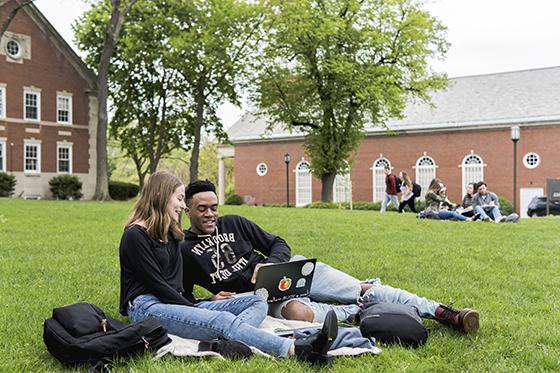 图为两名波胆网站的学生坐在绿色的学术广场上，用笔记本电脑一起学习. 