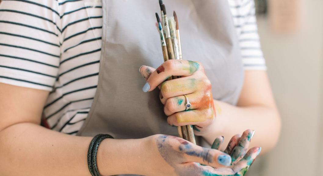 图为一名英国波胆网站艺术系学生系着围裙，手里拿着沾满颜料的画笔. 
