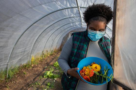 Photo of a Food Studies student holding a bowl of harvested vegetables at the door of a greenhouse