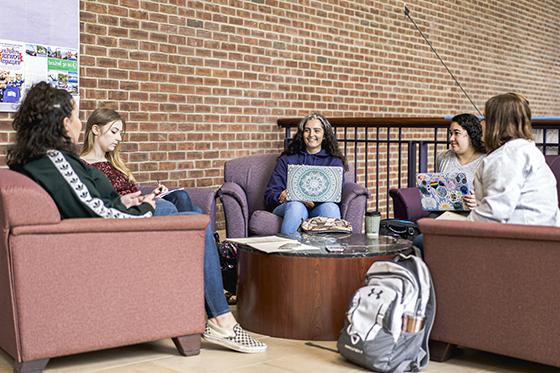 图为五名波胆网站的学生坐在教室外的椅子上，一边用笔记本电脑工作，一边聊天