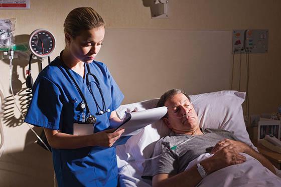 一个护士穿着手术服，在写字板上写字，旁边是一个熟睡的病人