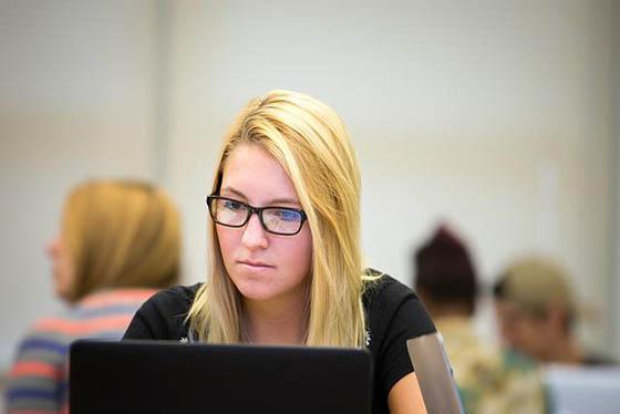 一个戴着眼镜的金发女人在教室里用电脑工作的照片
