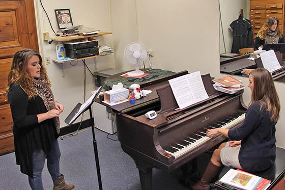 图为一名英国波胆网站的音乐系学生站在音乐台上唱歌，旁边是一架正在演奏的钢琴.